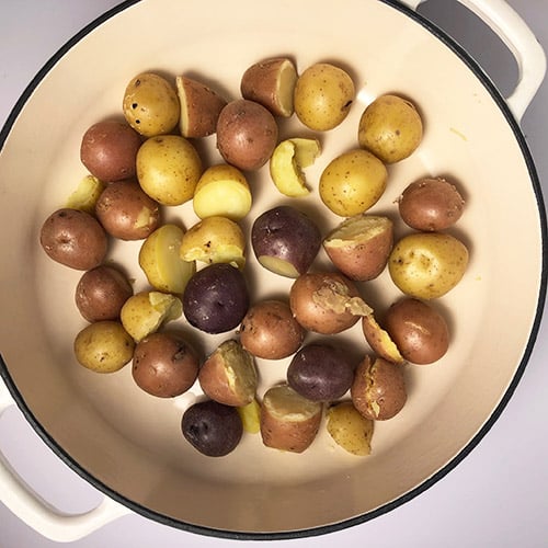 Top-down view of cooked baby potatoes in a white pot. 