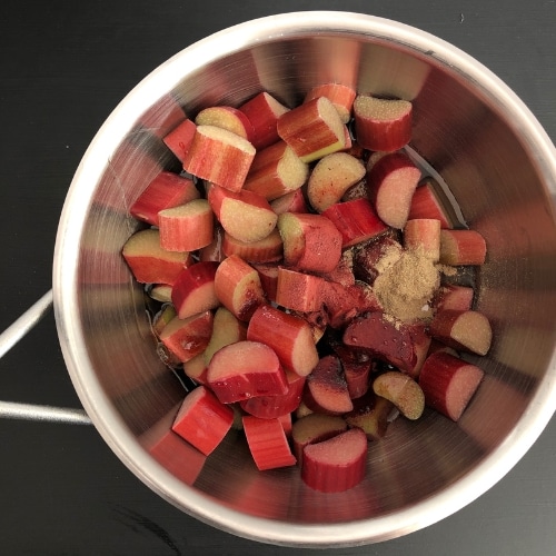 Top-down view of chopped rhubarb, maple syrup, cardamom and beetroot powder in a medium saucepan.