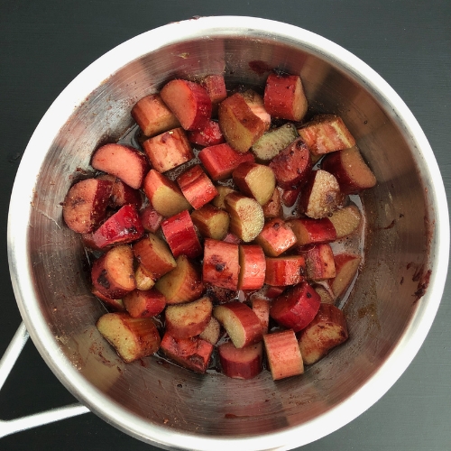 Top-down view of chopped rhubarb, maple syrup, cardamom and beetroot powder in a medium saucepan, bring to a boil.