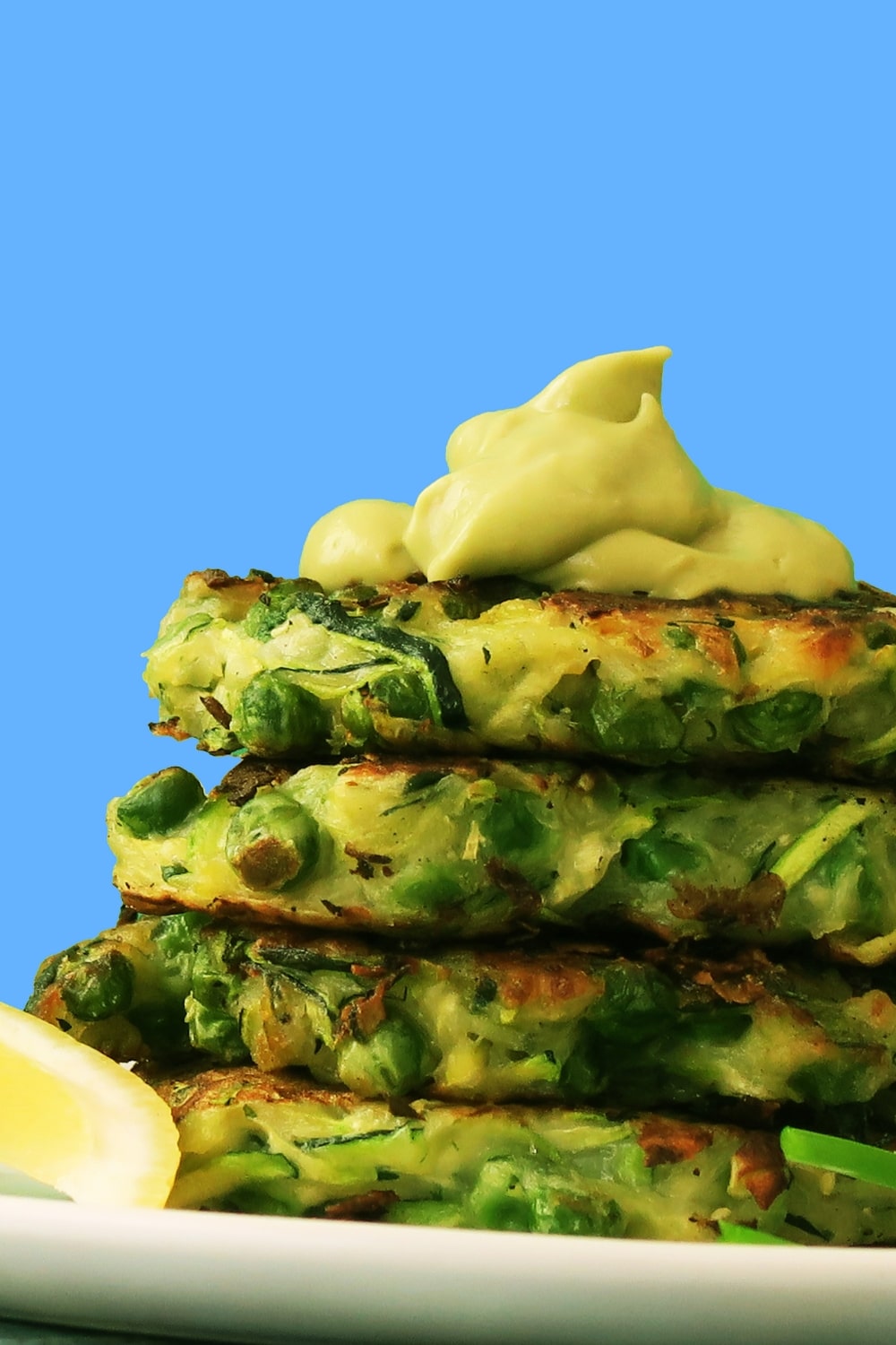 Side-view of stacked Zucchini and Green Pea Fritters topped with avocado crema