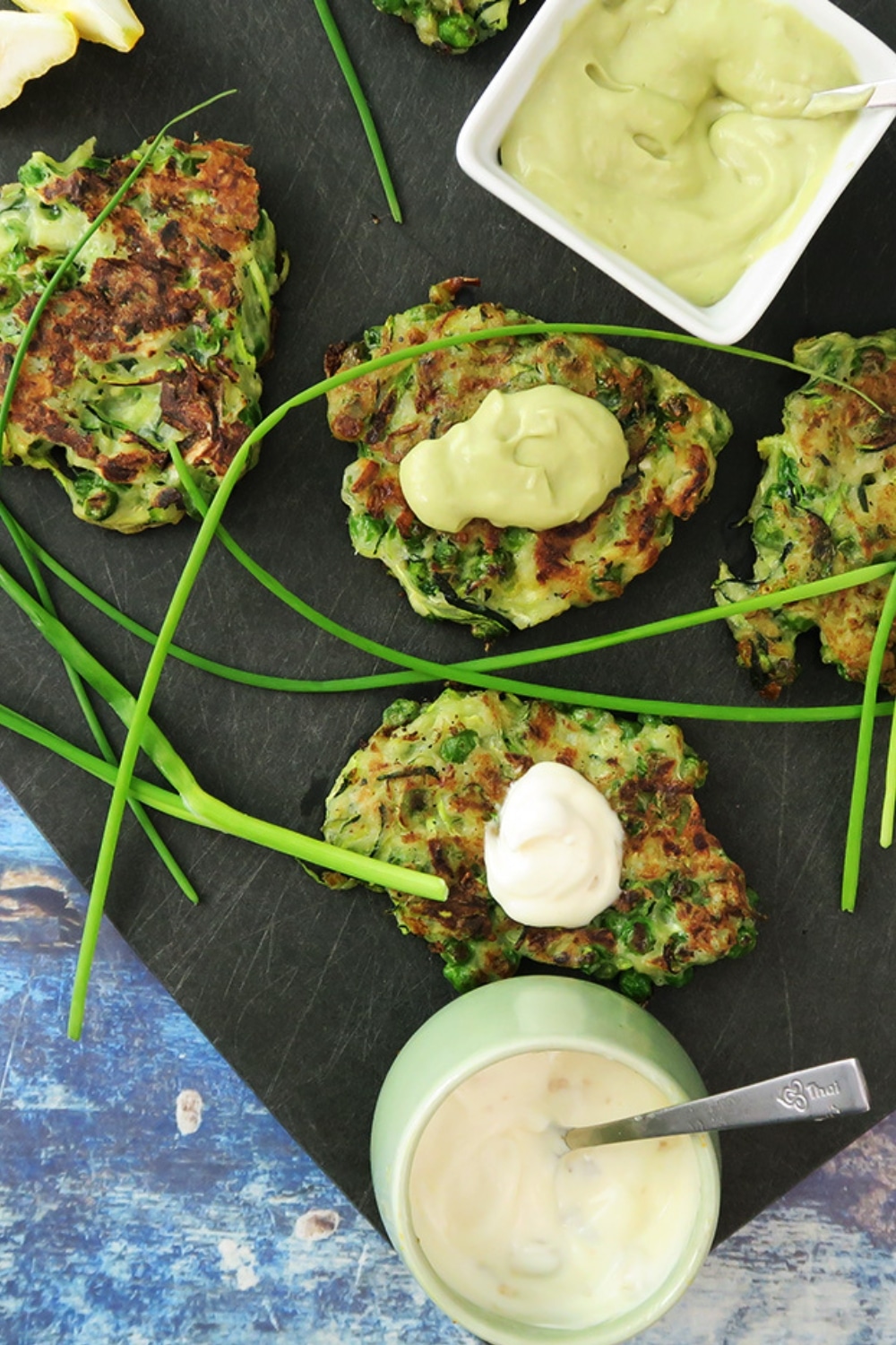 Top-down view of Zucchini and Green Pea Fritters topped with avocado crema