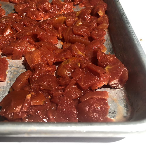 Close up of diced canned tomatoes on a baking sheet, before roasting.