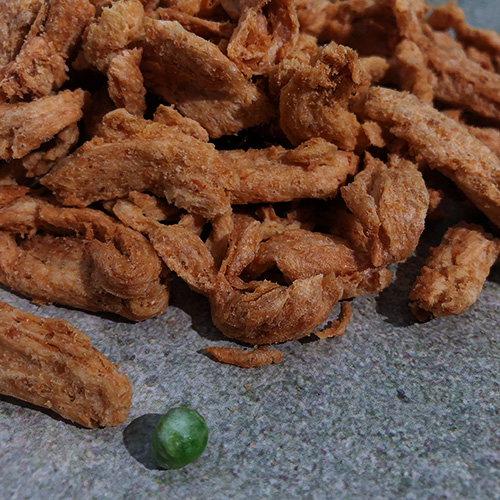 Close up view of dry (not rehydrated) soy curls, along with a green pea for perspective on size 