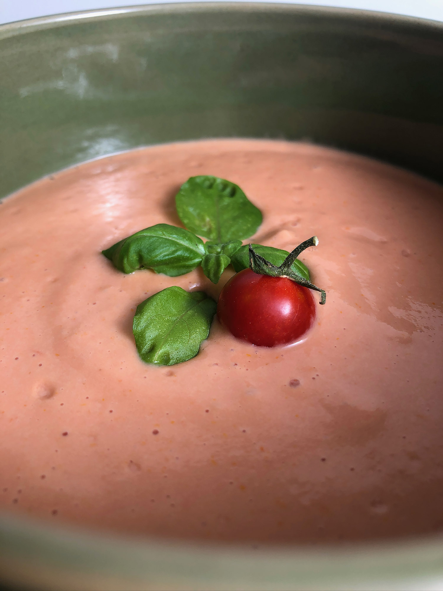 Low angle view of sun-dried tomato soup, topped with fresh basil and a teeny, tiny tomato