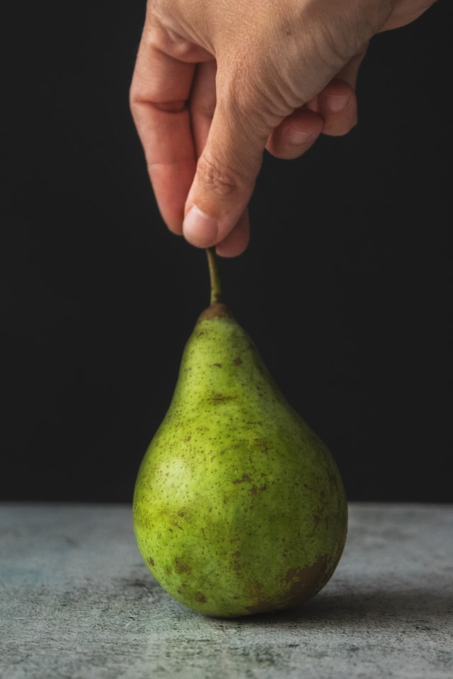Decorative: Hand holding the stem of a pear