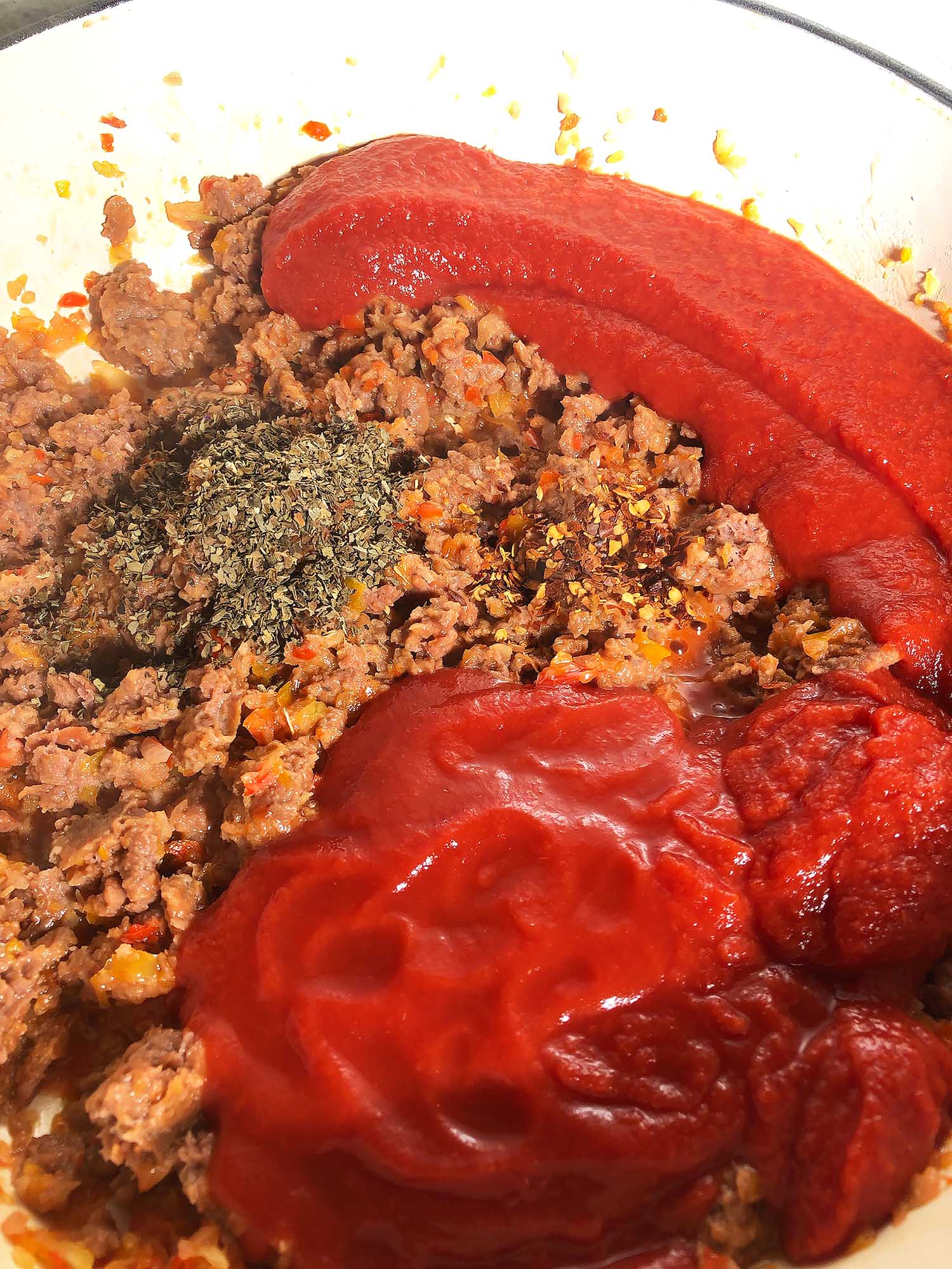 Top-down view of strained tomatoes, and spices added to sauce
