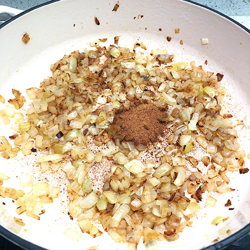 Coconut sugar added to caramelized onions in a white cast iron pan.