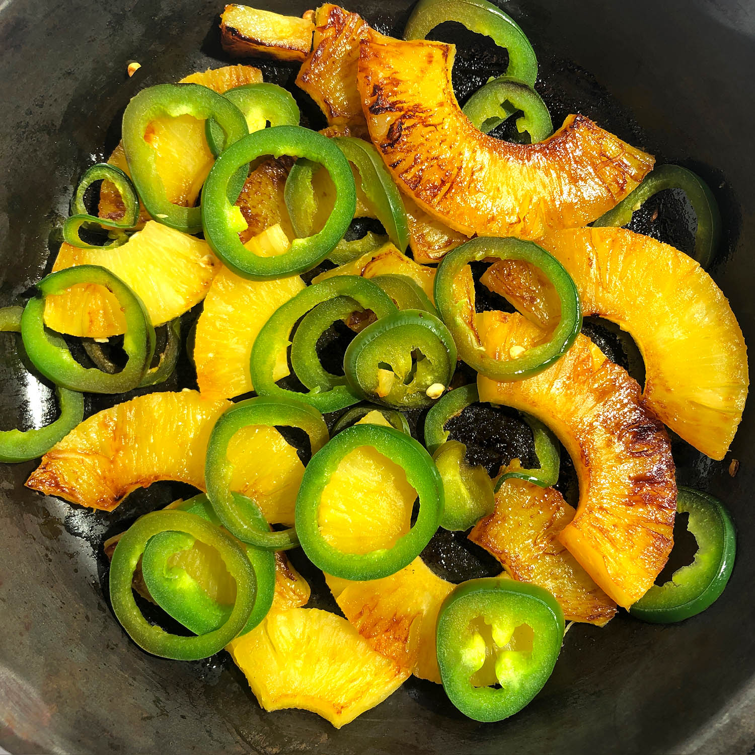 Top-down view of caramelized pineapple and jalapeno in a frying pan
