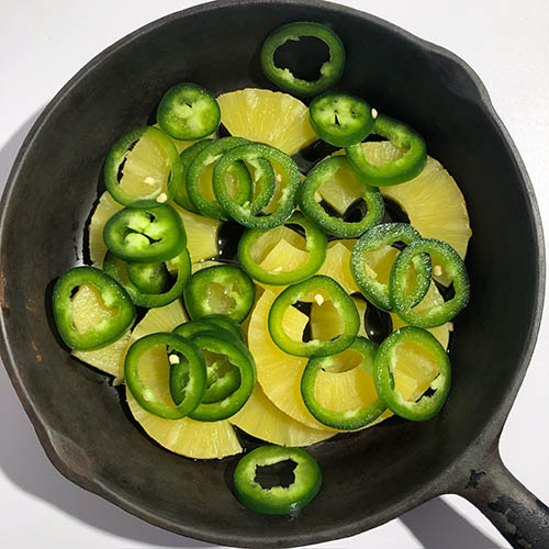 Top-down view of uncooked pineapple and jalapeno in a frying pan