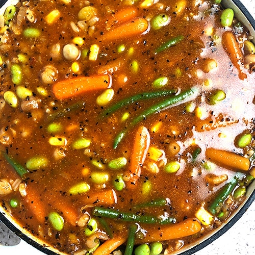 Top-down, close up view of Hearty Tomato Vegetable Soup, with vegetables, chickpeas, and edamame beans in a tomato broth