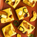 Pieces of Pineapple Jalapeno Cornbread topped with plant-based butter and decorated with jalapenos and pieces of caramelized pineapple