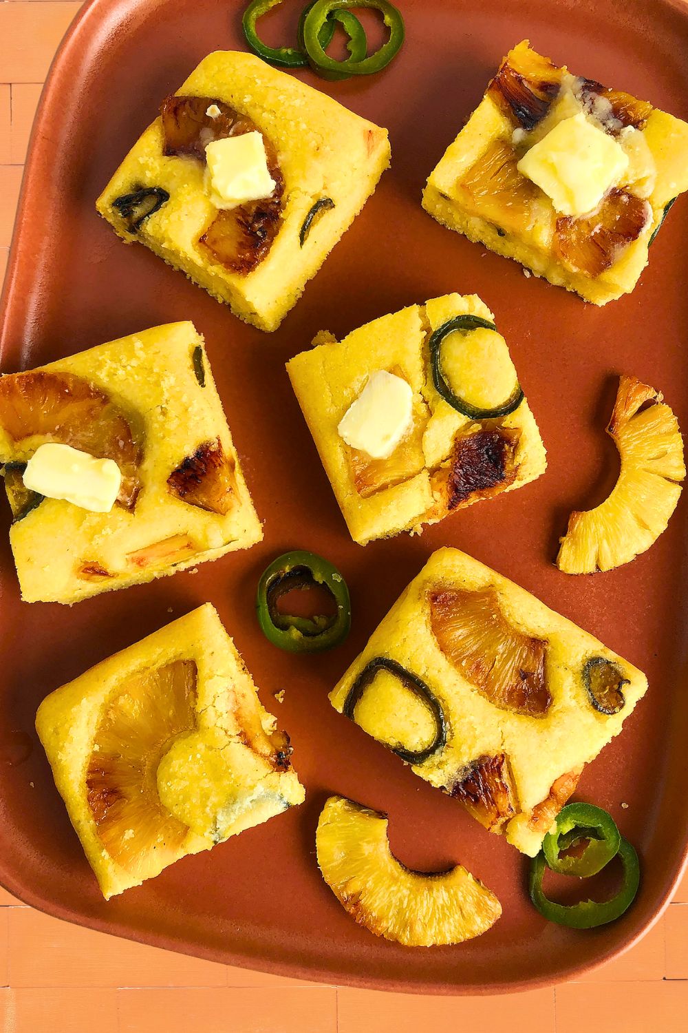 Pieces of Pineapple Jalapeno Cornbread topped with plant-based butter and decorated with jalapenos and pieces of caramelized pineapple