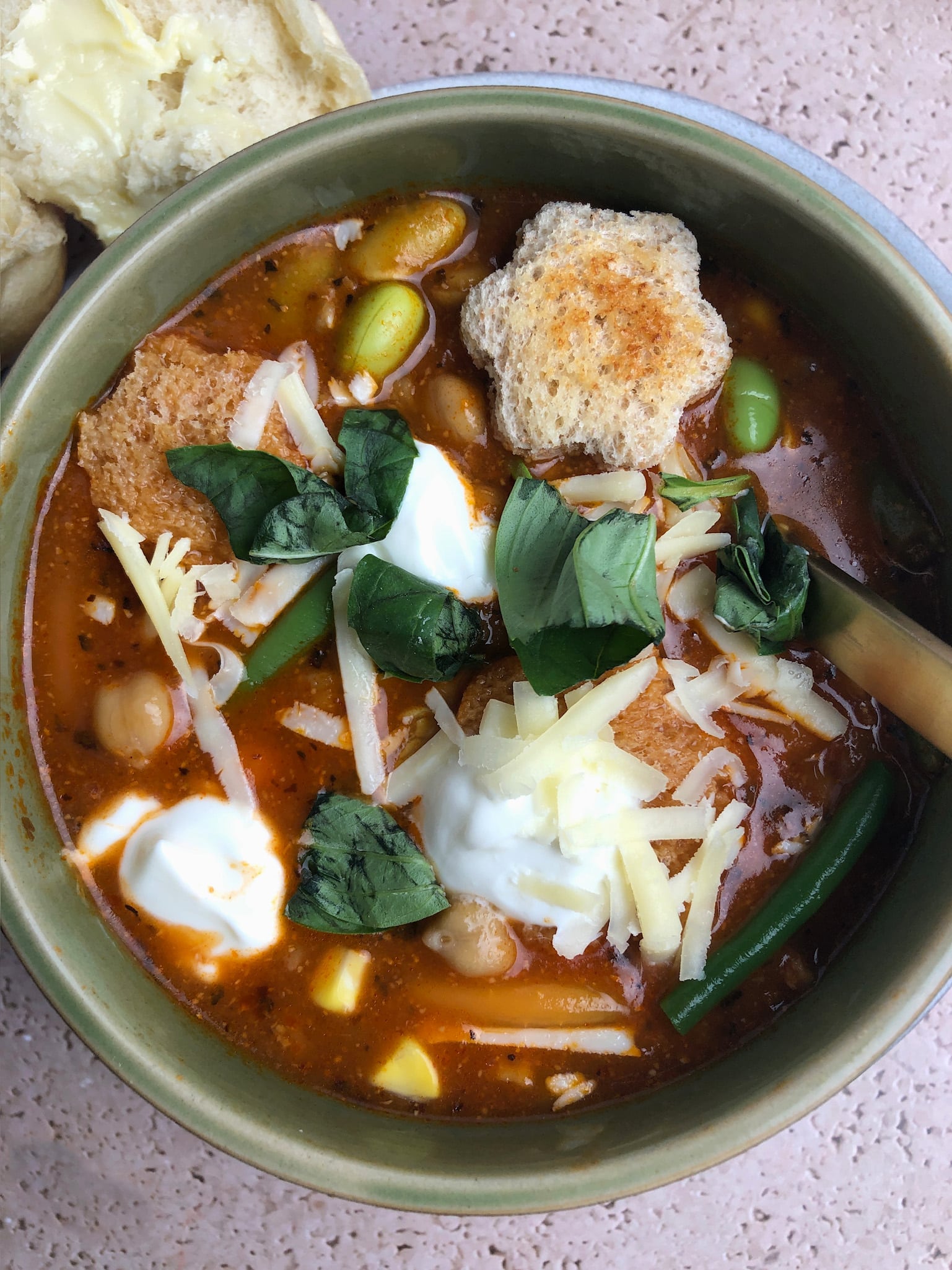 Top-down view of Hearty Tomato Vegetable Soup, topped with fresh basil, sour cream, and croutons