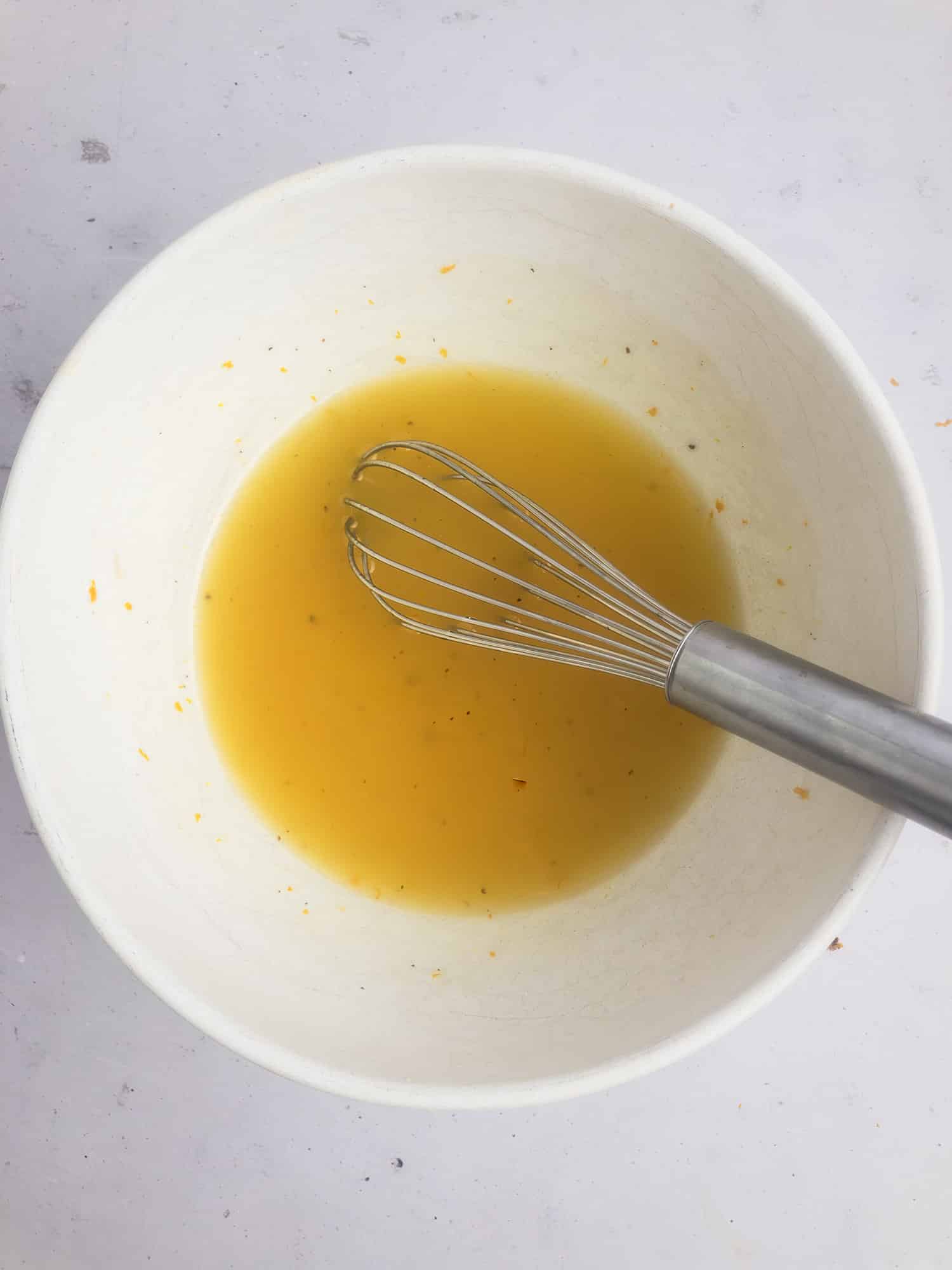 Top-down view of finished orange vinaigrette in a mixing bowl with a whisk