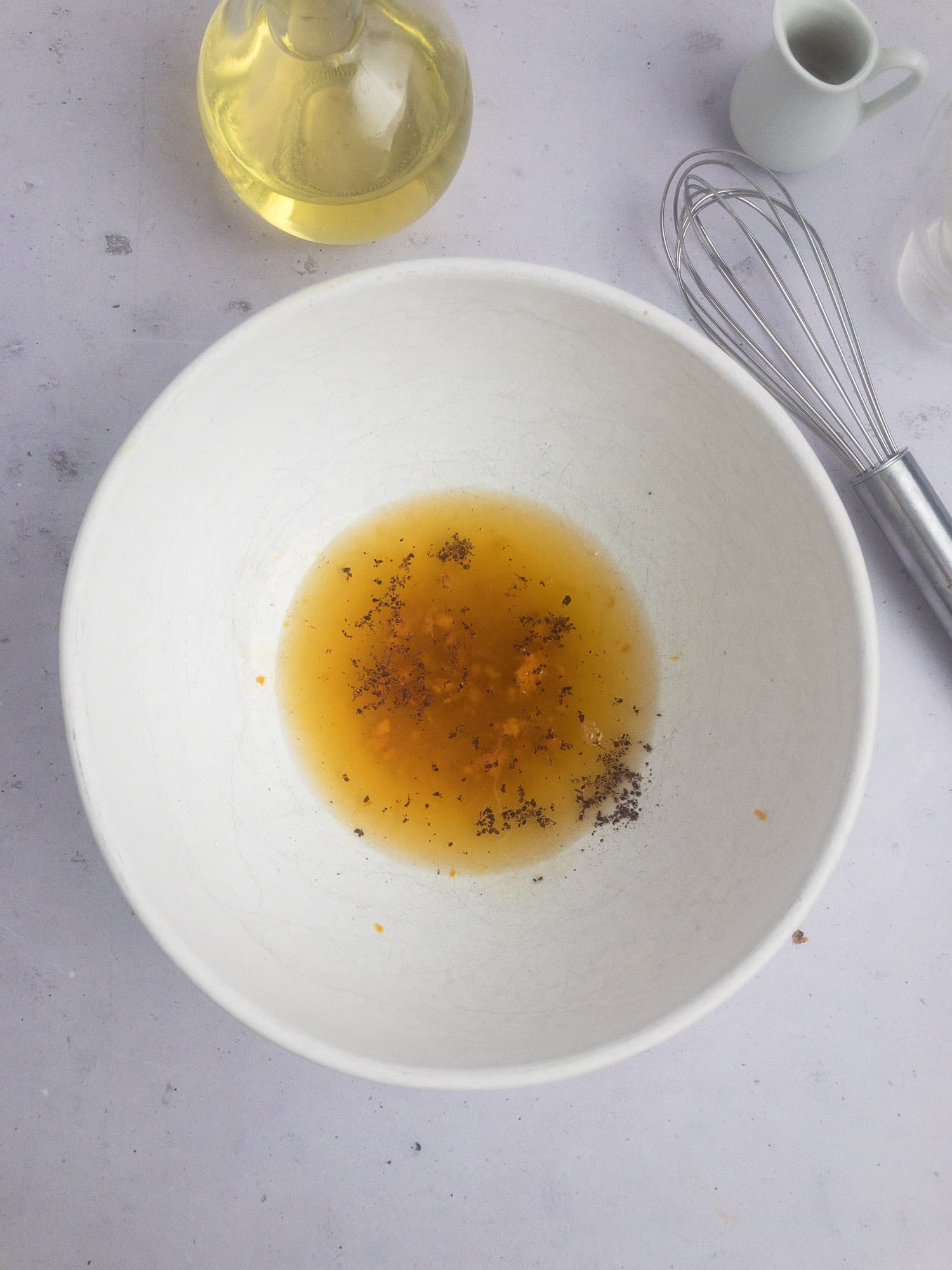 Top-down view of white bowl with ingredients for orange vinaigrette, including orange juice, maple syrup, orange zest, and sumac