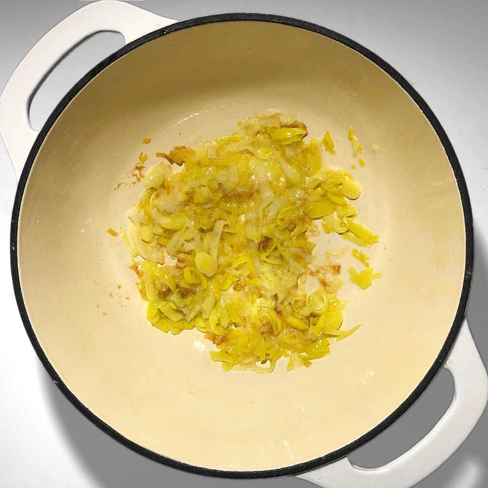 Top-down view of sauteed leeks in a white soup pot, with margarine