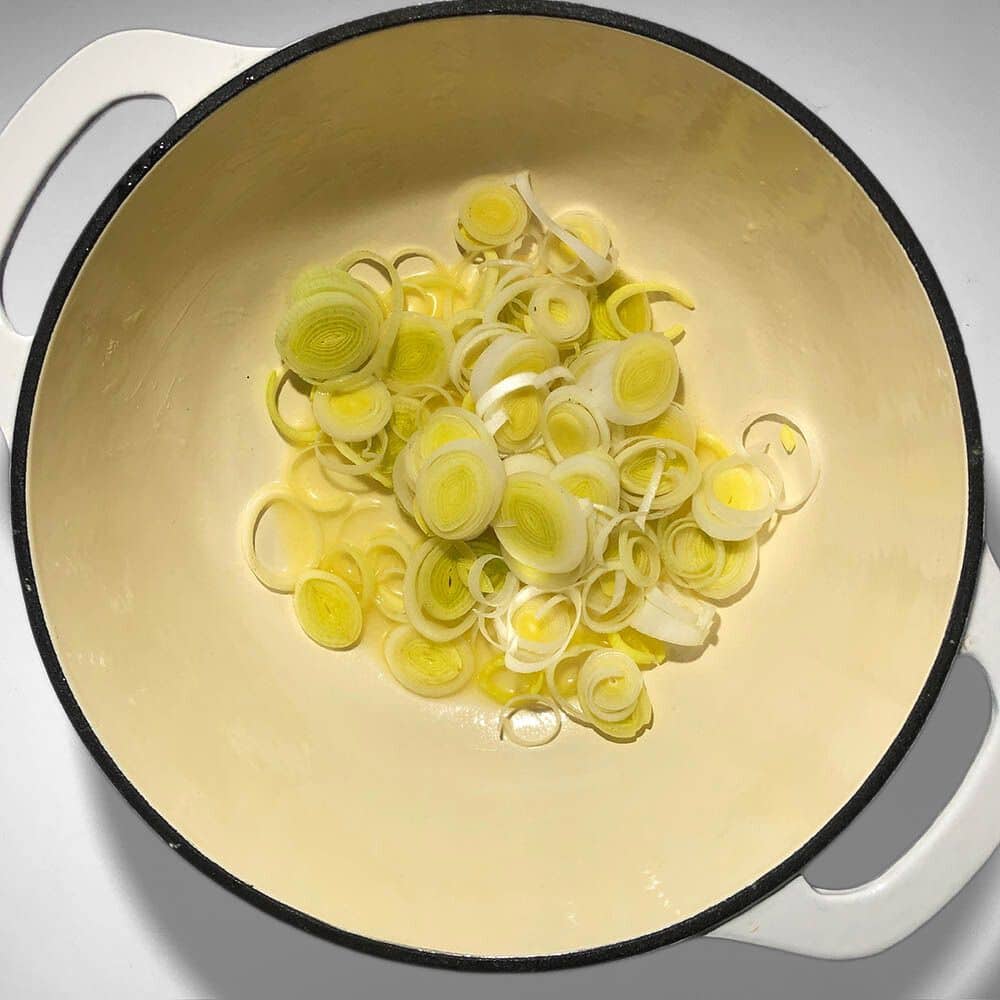 Top-down view of leeks in a white soup pot, with margarine