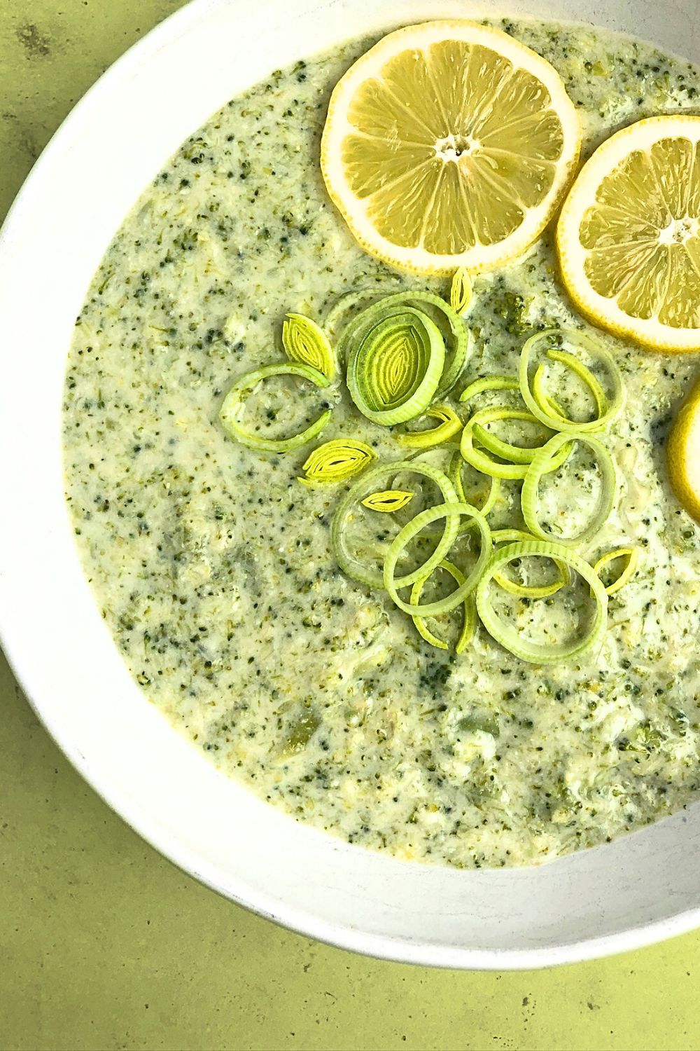 Top-down view of Lemony Leek and Broccoli Soup, showing a close-up view of the soup, garnished with lemons and thinly sliced leeks