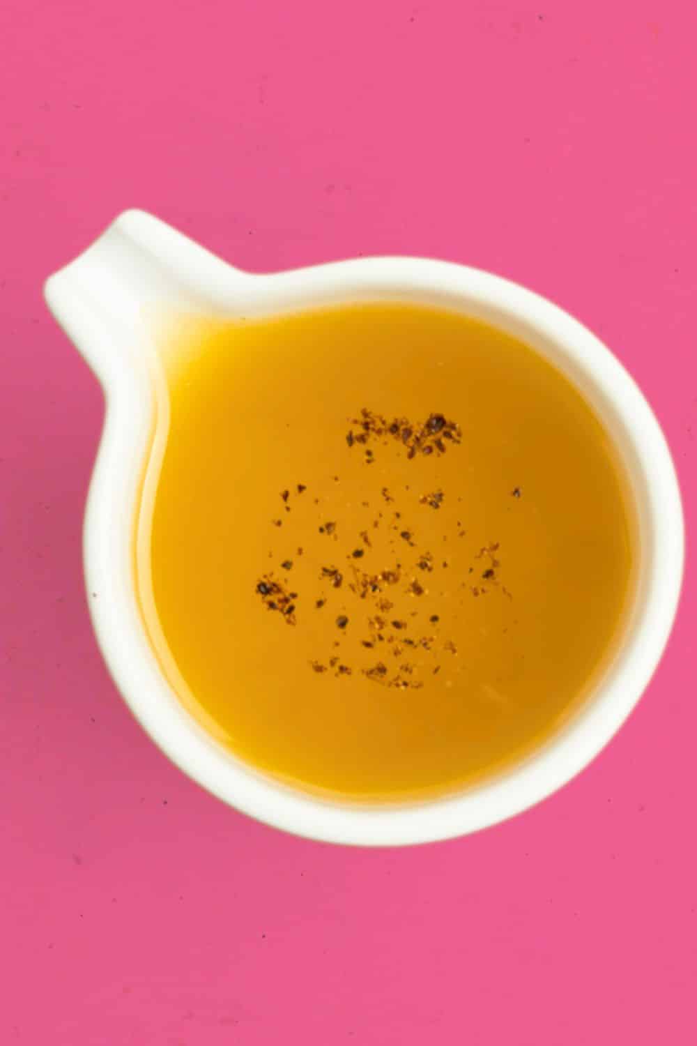 Top-down view of orange vinaigrette in a white container against a bright pink background