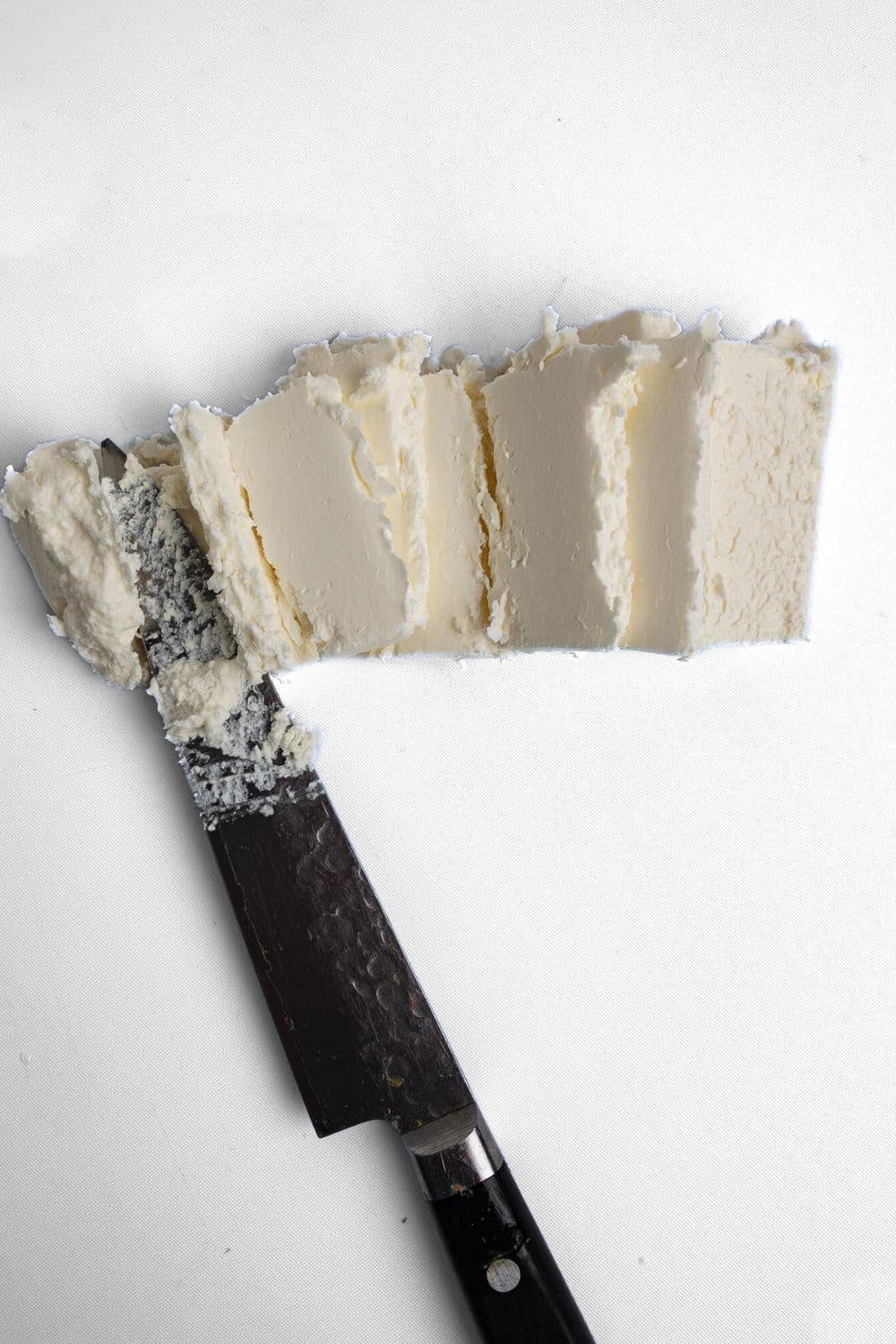 Top-down view of slicing feta on a white cutting board