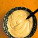 Top-down view of Smoky Maple Bacon Mayonnaise, in black bowl against a dark orange stone background