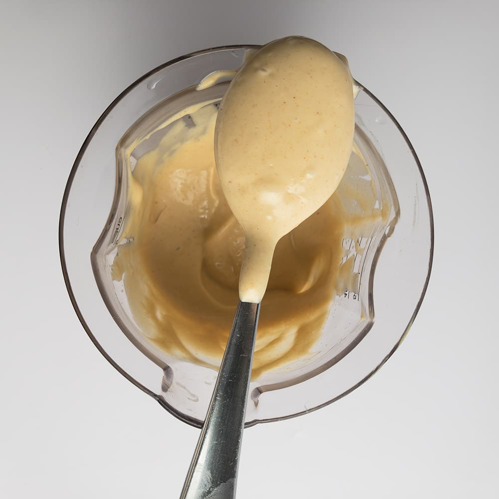 Top-down view of spoon with Smoky Maple Bacon Mayonnaise on top of a measuring cup