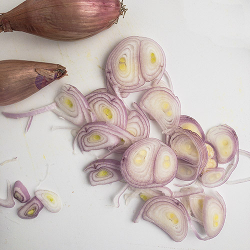 Top-down view of thinly sliced shallots on a white cutting board