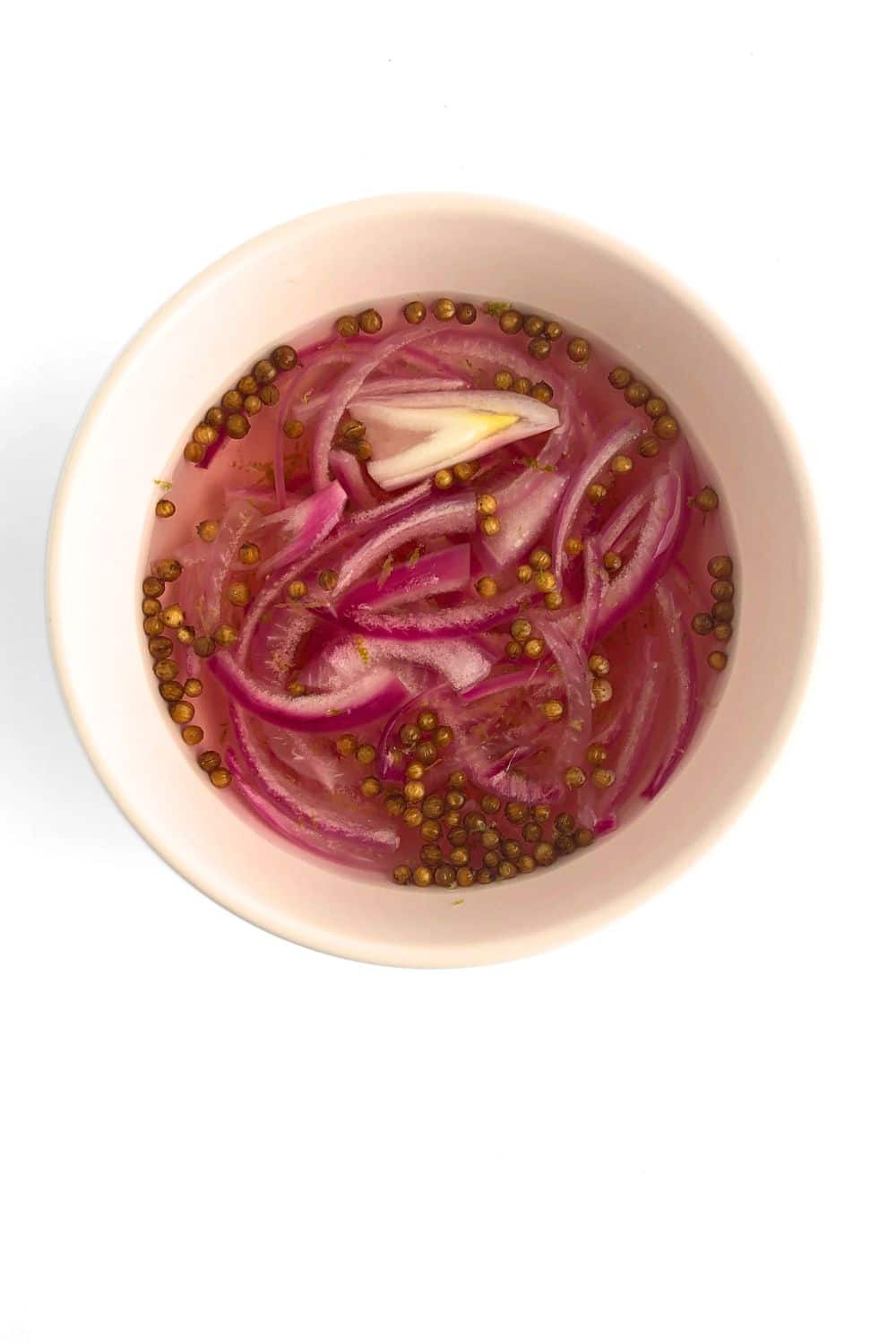 Top-down view of quick pickled onions in a pink bowl against a white background